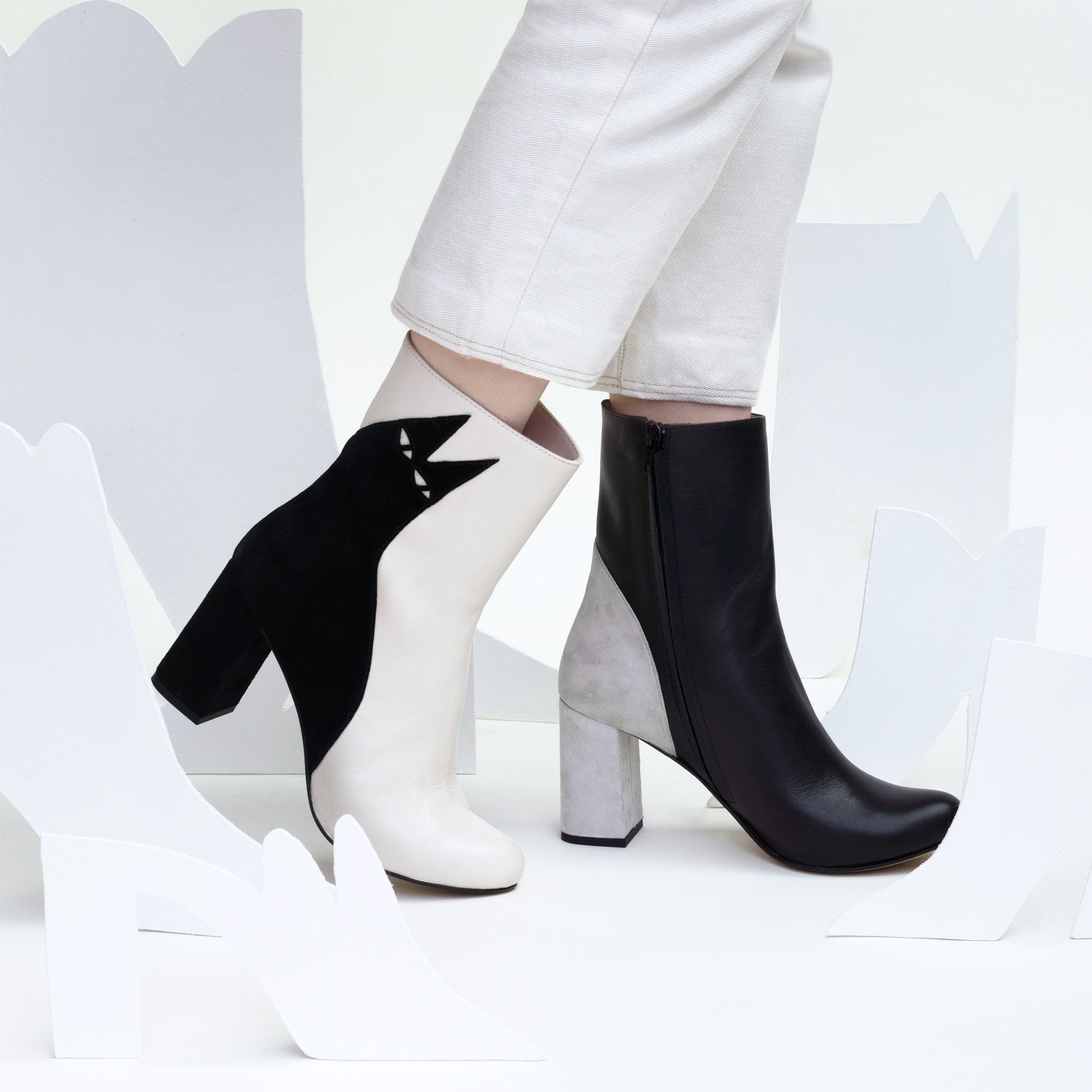 High heeled cat themed boots with simple elegant design modelled in white product shot set with white cut out shoes.
