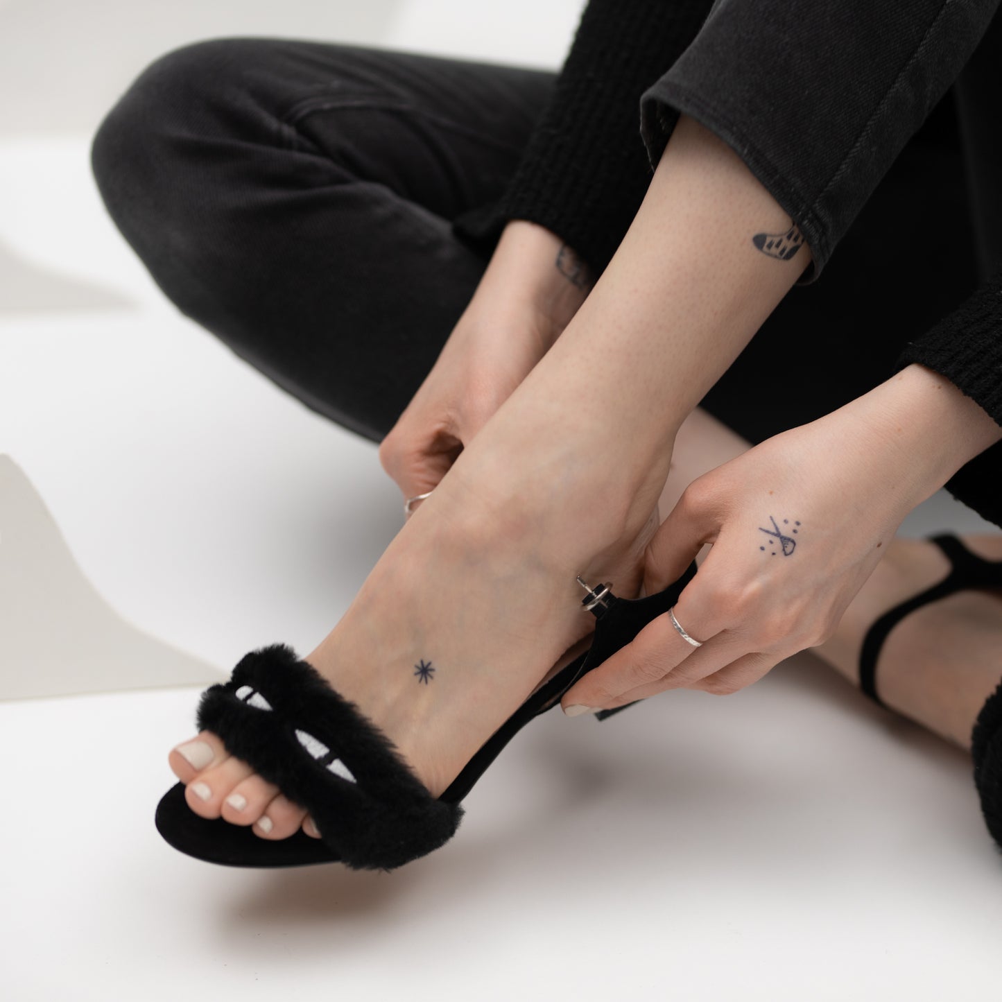 Model putting on a pair of black faux fur sandals showing off the cat eye strap.